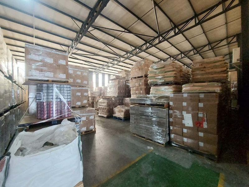 Spacious industrial warehouse interior featuring high exposed steel roof trusses and durable concrete flooring, currently utilized for bulk storage.