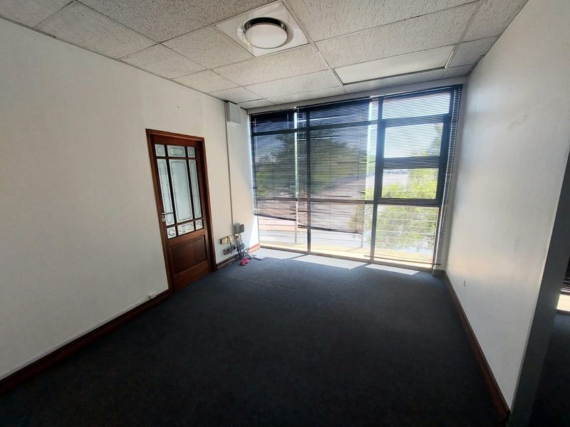 A vacant office space featuring a suspended ceiling, large window with blinds, and timber door, suitable for a professional workspace.