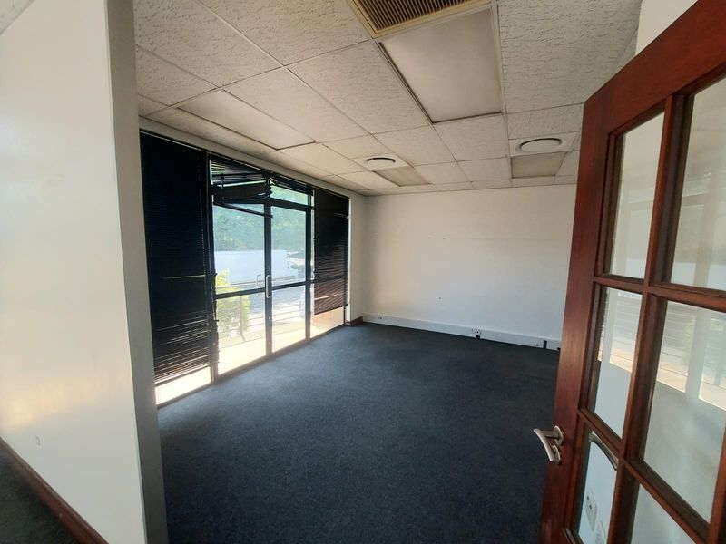 An empty office space featuring a suspended ceiling, recessed lighting, carpet flooring, and a glass sliding door with venetian blinds.