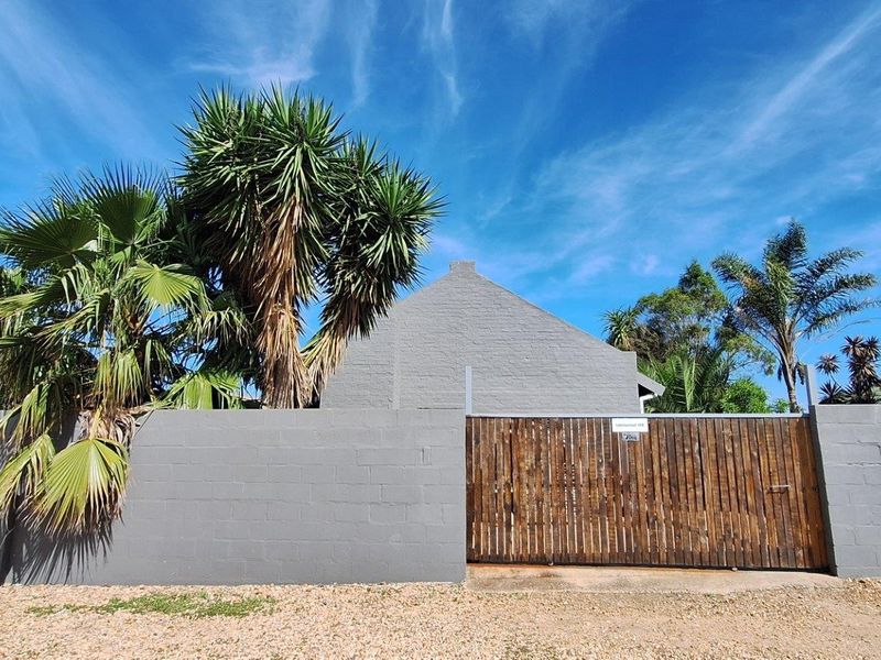 Front exterior view of the townhouse featuring a painted masonry boundary wall, timber entrance gate, and gravel driveway area.