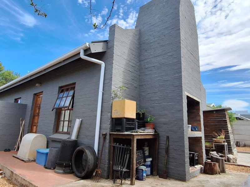 Rear exterior view of the townhouse featuring a built-in brick braai, chimney, and concrete patio area.