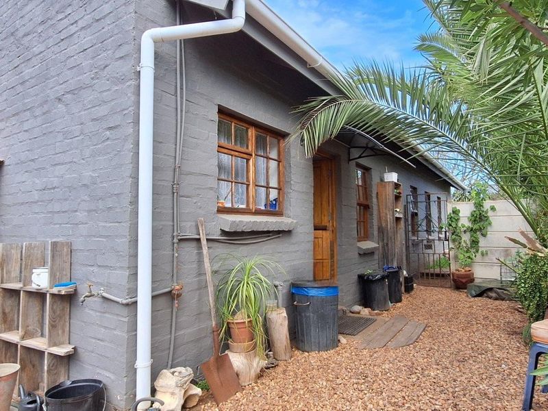Rear exterior view of the townhouse featuring painted brick walls, timber window frames, and a gravel courtyard area.