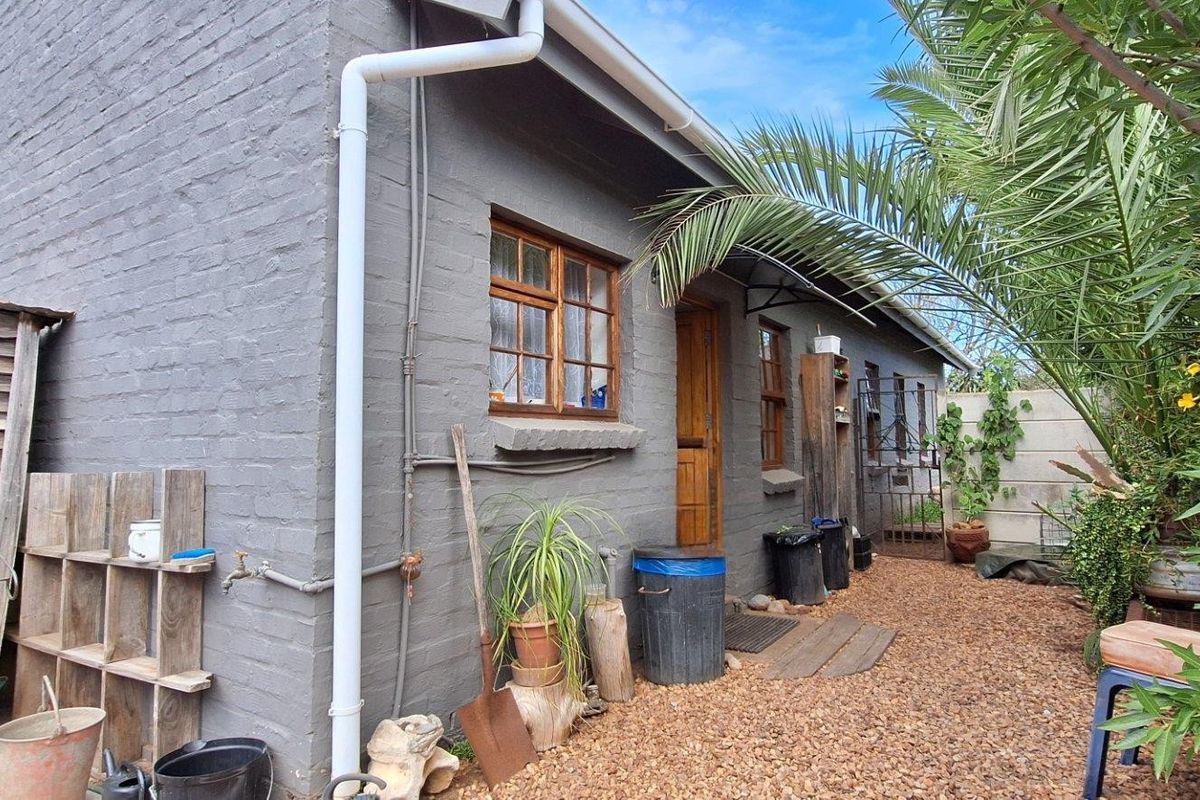 Rear exterior view of the townhouse featuring painted brick walls, timber window frames, and a gravel courtyard area.