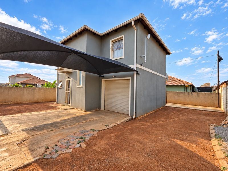 Exterior view of a two-story house featuring a single garage, security gate, and a shade sail over the concrete driveway area.