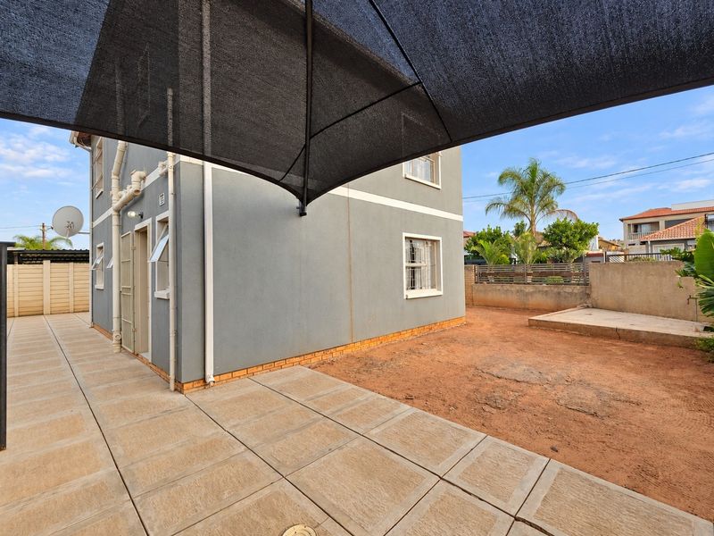 Rear exterior view featuring a paved patio area, shade sail, and an unlandscaped garden space with boundary walling.