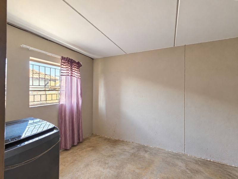 A functional laundry space featuring concrete flooring, security bars on the window, and a simple panel ceiling, ready for finishing or utility use.