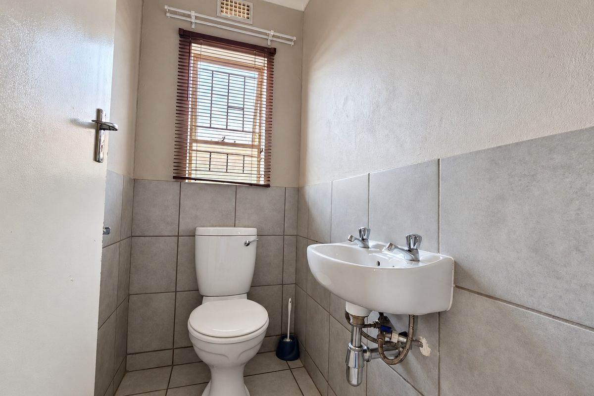 A compact bathroom featuring a wall-mounted basin, toilet, and neutral tiled finishes, providing a functional and clean space.