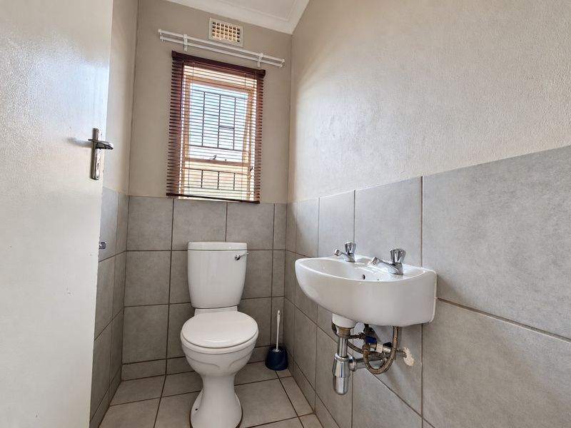 A compact bathroom featuring a wall-mounted basin, toilet, and neutral tiled finishes, providing a functional and clean space.