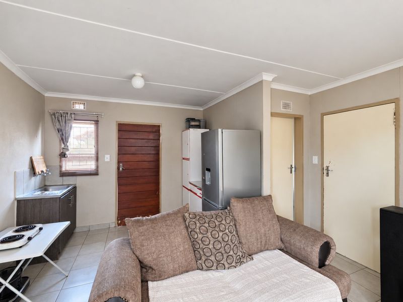 Open plan living area featuring tiled flooring, a compact kitchenette with sink, and access to multiple internal rooms.