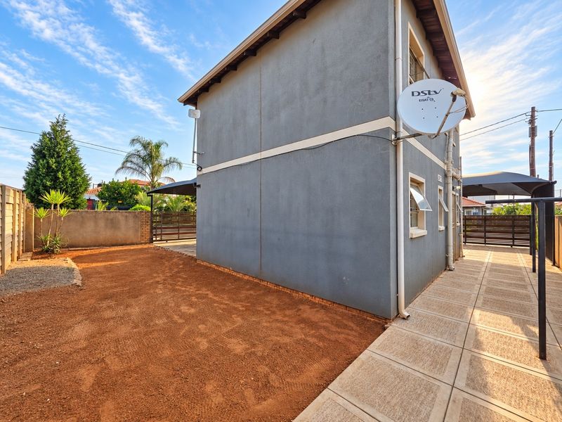 Rear view of the property featuring a paved walkway, satellite dish, and a side garden area with boundary walling.