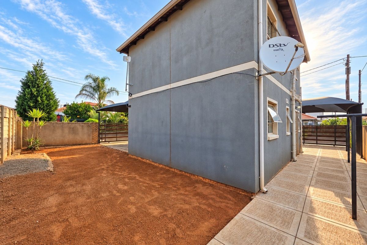 Rear view of the property featuring a paved walkway, satellite dish, and a side garden area with boundary walling.