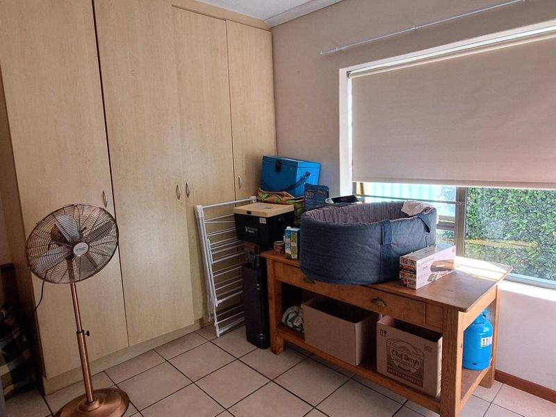 A bedroom featuring built-in cupboards, tiled flooring, and a window with a roller blind, offering a functional space with potential for modernization.