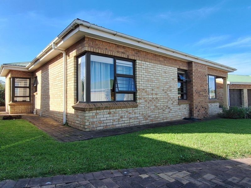 A well-maintained townhouse exterior featuring face brick construction, aluminium window frames, and a neat surrounding lawn with paved pathways.