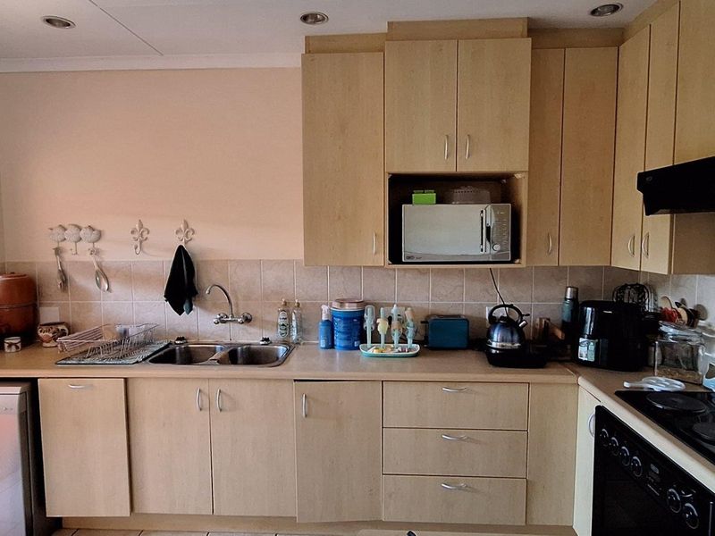 A functional kitchen featuring light wood-finish cabinetry, a double bowl sink, built-in oven, electric hob, and tiled backsplash with recessed lighting.