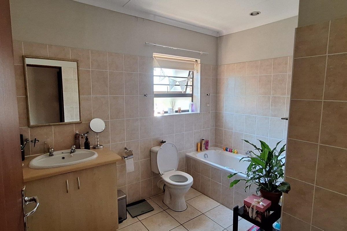 A functional bathroom featuring a built-in bathtub, vanity cabinet with basin, and neutral wall and floor tiling.