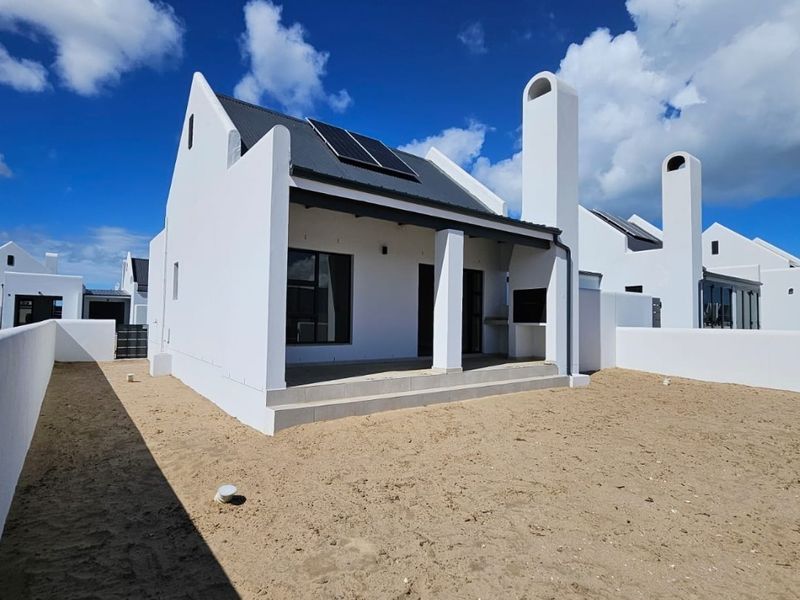 Rear view of a modern white house featuring a covered patio with a built-in braai, solar panels, and an expansive unlandscaped garden area.