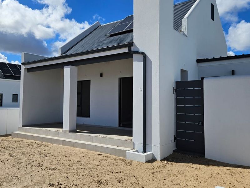 Modern house exterior featuring a covered patio, corrugated metal roof with solar panels, and a private side gate entrance.