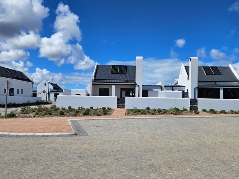 Modern residential estate featuring white facades, dark metal roofing, solar panels, and paved driveway access in a well-maintained suburban setting.