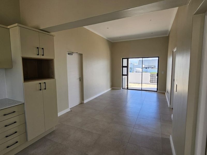Modern open-plan living area featuring tiled floors, neutral walls, and a compact kitchen with built-in appliances, leading to an outdoor space.