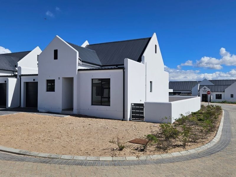 Modern residential property featuring a clean white facade, gabled roofline, and paved driveway in a well-maintained estate setting.