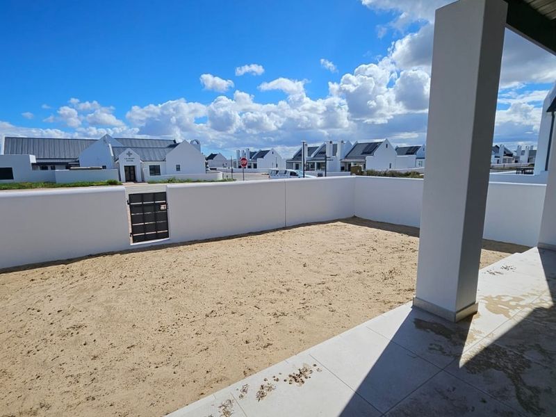 A covered patio area featuring tiled flooring and a perimeter wall, overlooking an unlandscaped sandy garden space.