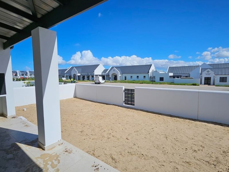 A covered patio area featuring a built-in braai and tiled flooring, overlooking an open, unfinished garden space with boundary walling.