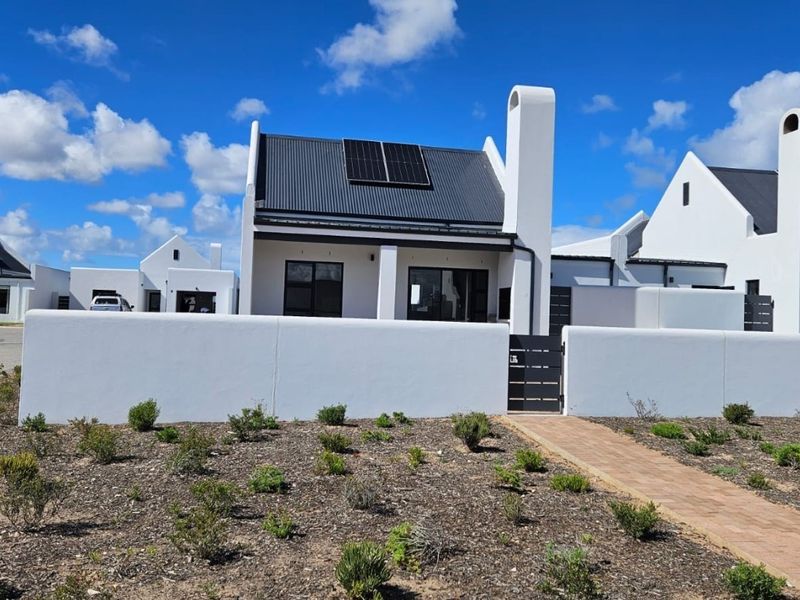 Modern single-story house featuring a white facade, metal roof with integrated solar panels, external chimney, and a private paved entrance.