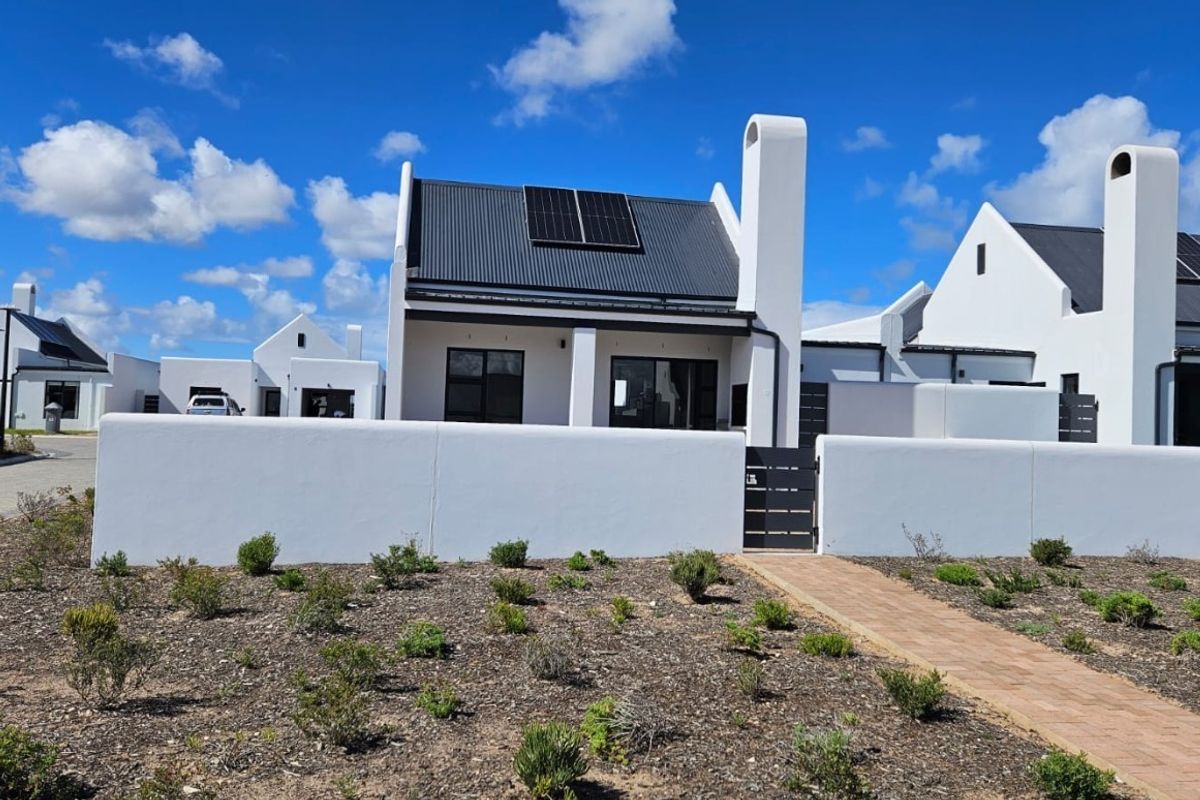 Modern single-story house featuring a white facade, metal roof with integrated solar panels, external chimney, and a private paved entrance.