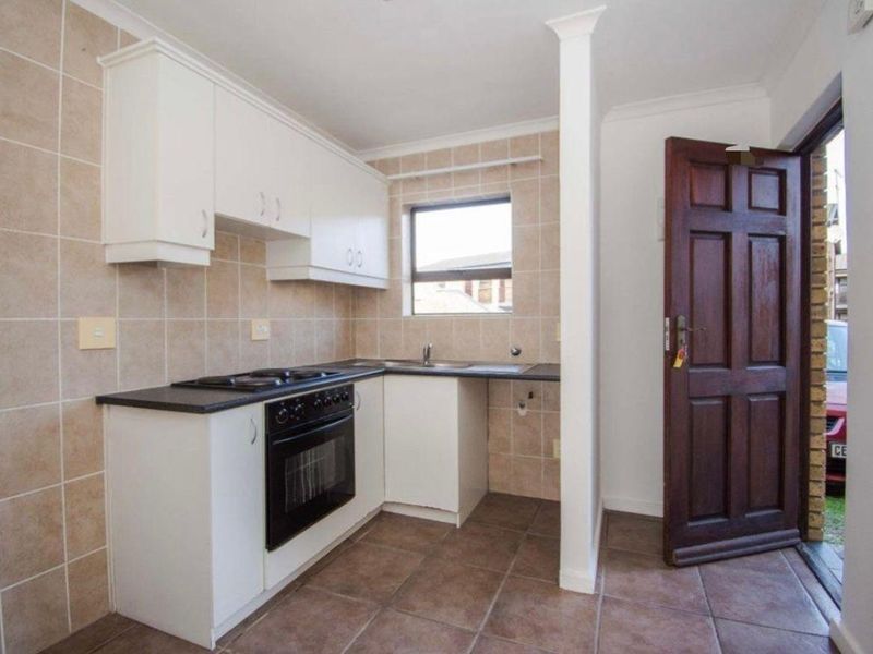 A functional kitchen featuring white cabinetry, dark countertops, built-in oven and hob, tiled splashbacks, and direct access to the exterior.