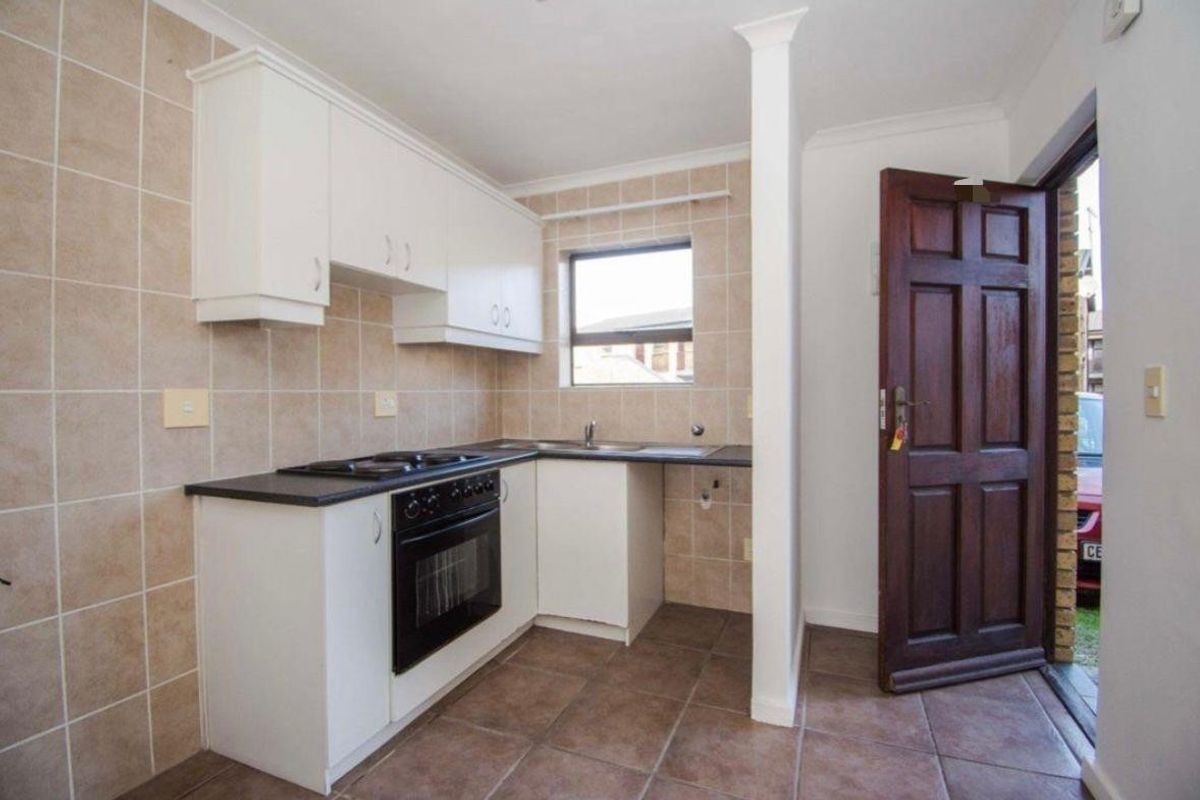 A functional kitchen featuring white cabinetry, dark countertops, built-in oven and hob, tiled splashbacks, and direct access to the exterior.