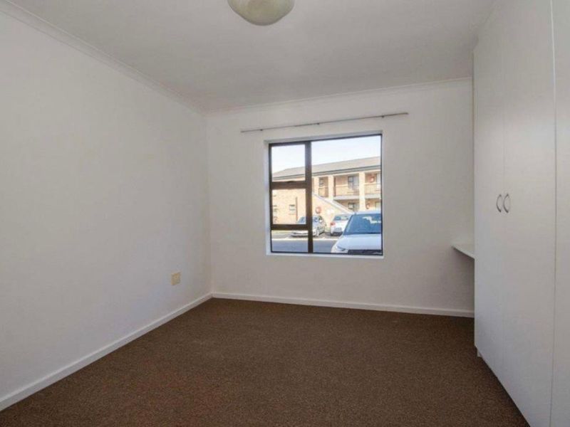 A clean, empty bedroom featuring neutral carpeting, built-in storage cupboards, and a window providing natural light.