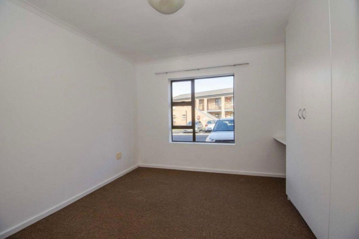 A clean, empty bedroom featuring neutral carpeting, built-in storage cupboards, and a window providing natural light.