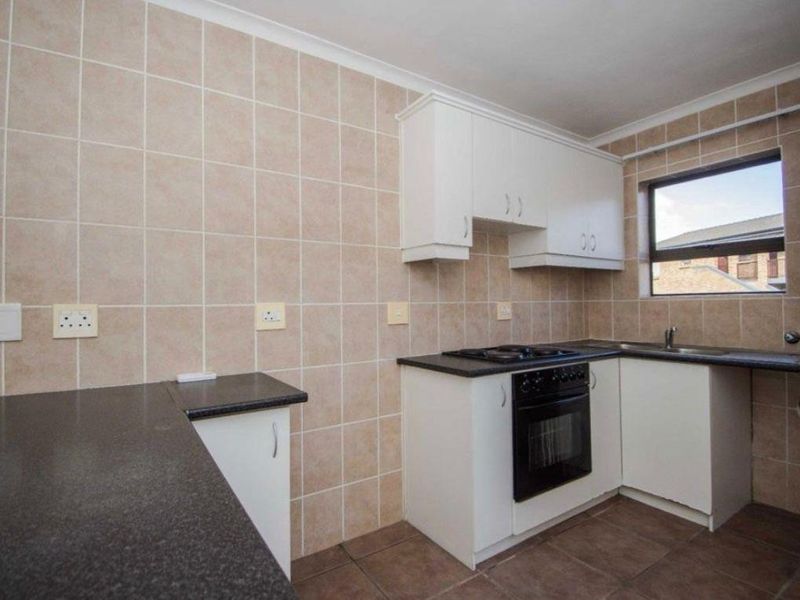 A functional kitchen featuring white cabinetry, dark laminate countertops, built-in oven and hob, tiled splashbacks, and tiled flooring.