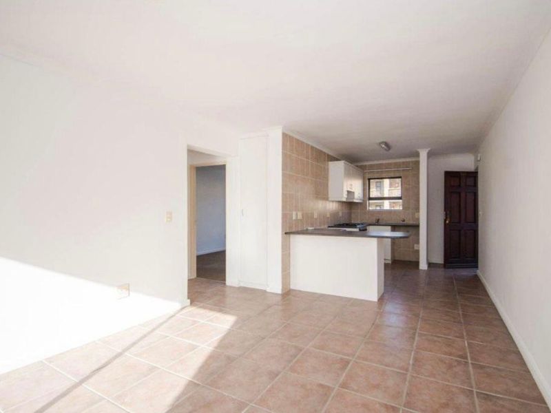 An open-plan living and kitchen area featuring tiled flooring, a breakfast bar, and functional kitchen cabinetry with a built-in stove.