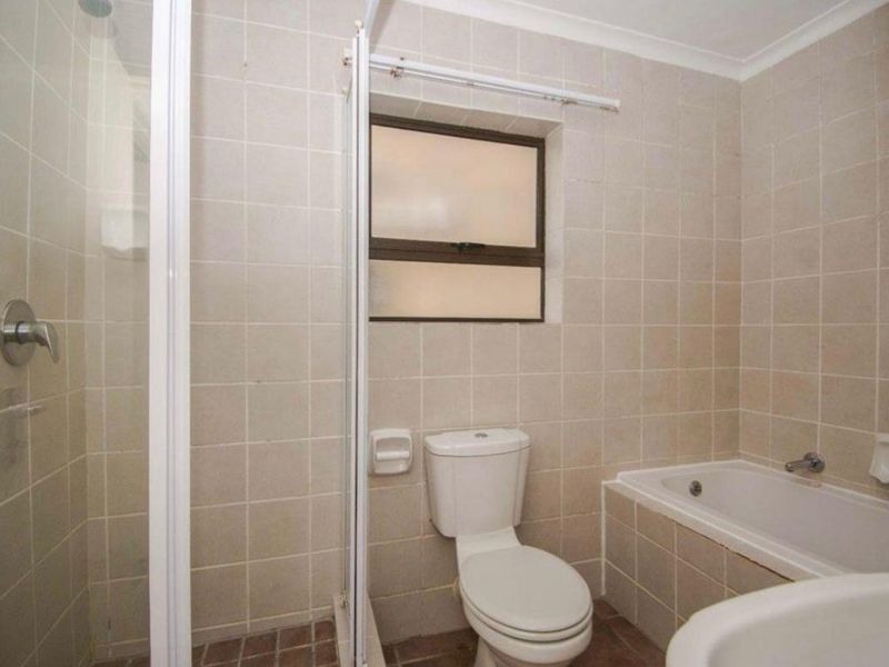 A functional bathroom featuring a built-in bathtub, separate shower enclosure, and toilet, finished with neutral wall tiling.