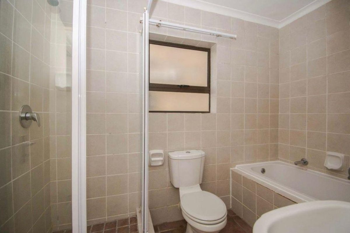 A functional bathroom featuring a built-in bathtub, separate shower enclosure, and toilet, finished with neutral wall tiling.