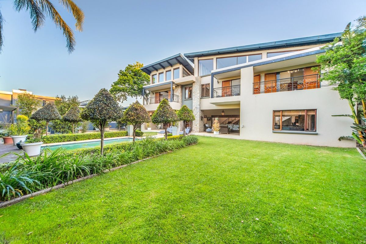 A spacious rear exterior view of a multi-story modern home featuring a swimming pool, manicured lawn, and multiple balconies with stone architectural accents.