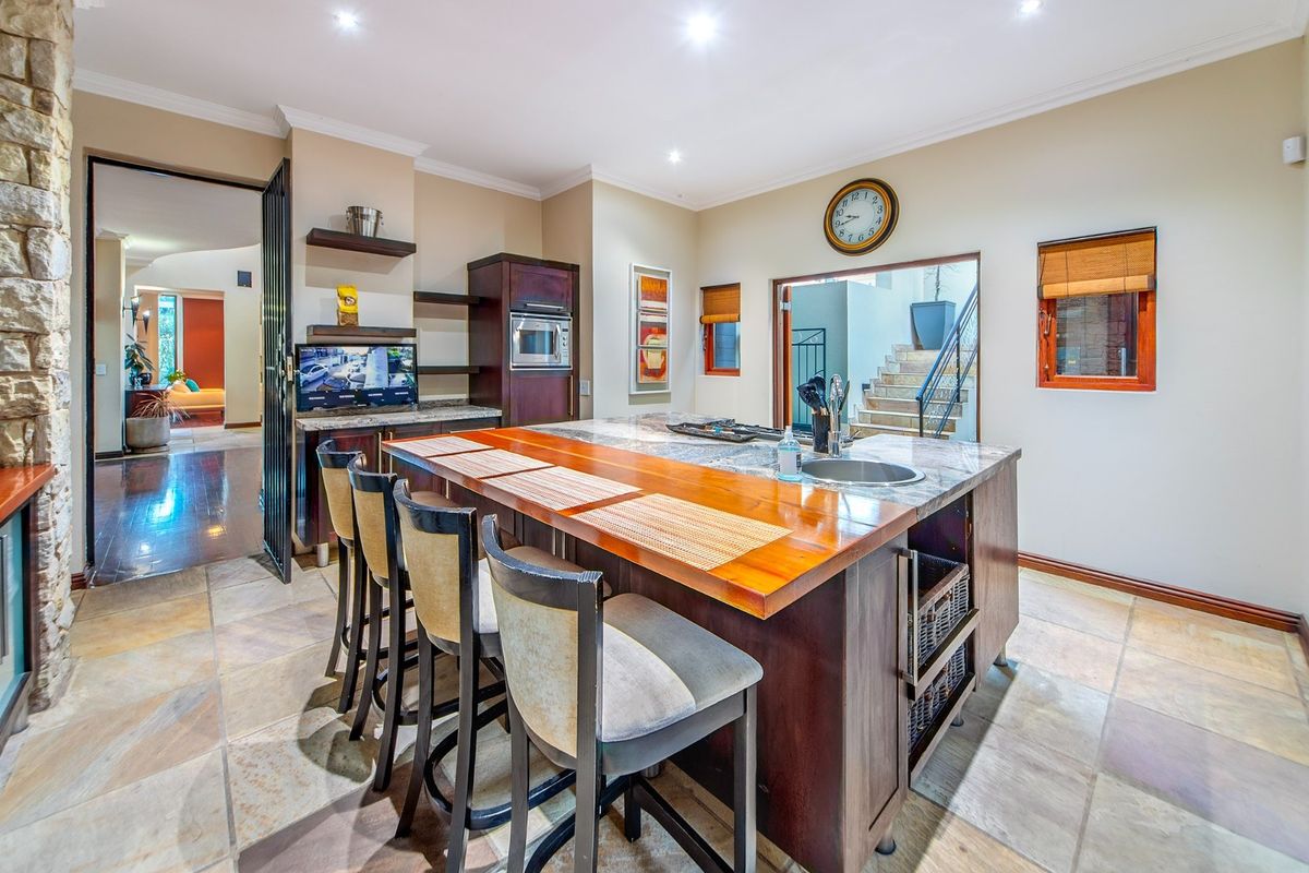 Spacious kitchen featuring a large island with stone countertops, a wooden breakfast bar, integrated appliances, and elegant stone flooring.