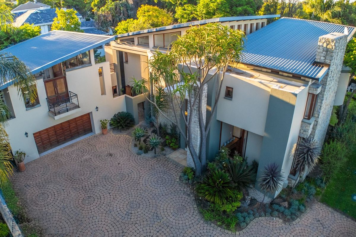 Aerial view of a modern multi-level residence featuring a paved circular driveway, stone accents, metal roofing, and integrated garage.