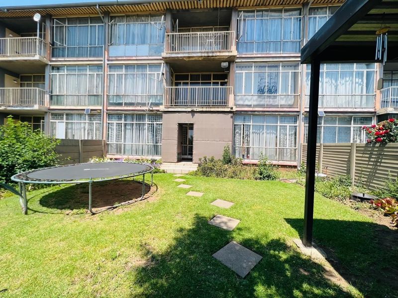 Rear view of a multi-story apartment building featuring private balconies, large windows, and a shared garden area with a stone pathway.