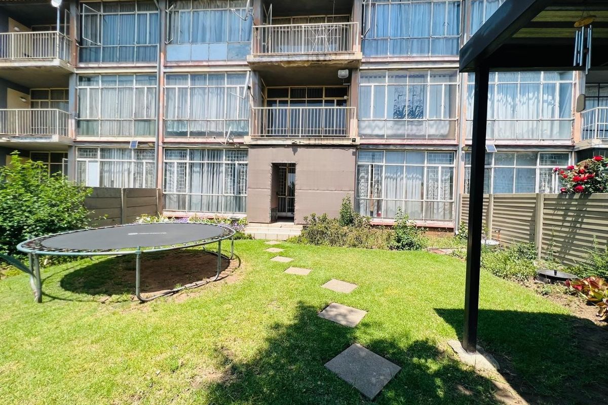 Rear view of a multi-story apartment building featuring private balconies, large windows, and a shared garden area with a stone pathway.