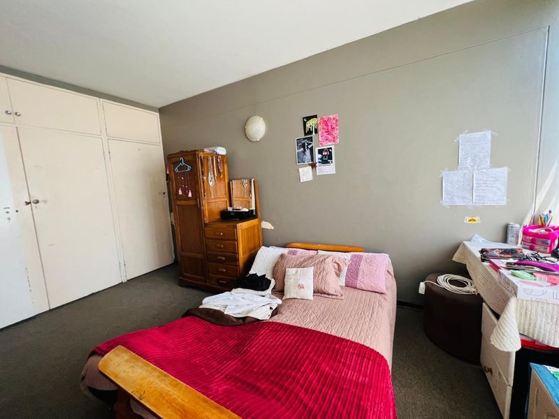 A bedroom featuring built-in cupboards and a wall-mounted light fixture, requiring minor cosmetic updates to the wall finishes.