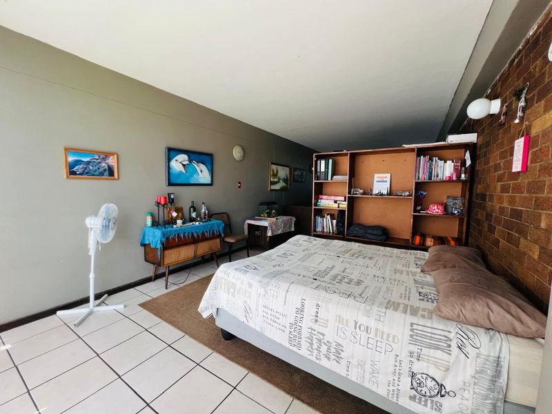 Spacious bedroom featuring tiled flooring and a distinctive exposed brick feature wall, offering a functional layout with ample space.
