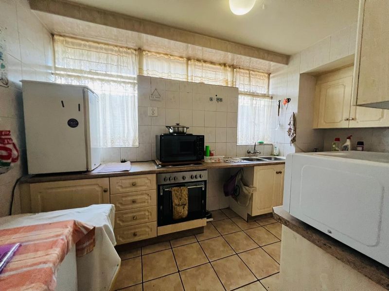 A functional kitchen featuring built-in cabinetry, tiled backsplash, and ceramic flooring, offering a dated aesthetic with potential for modern renovation.