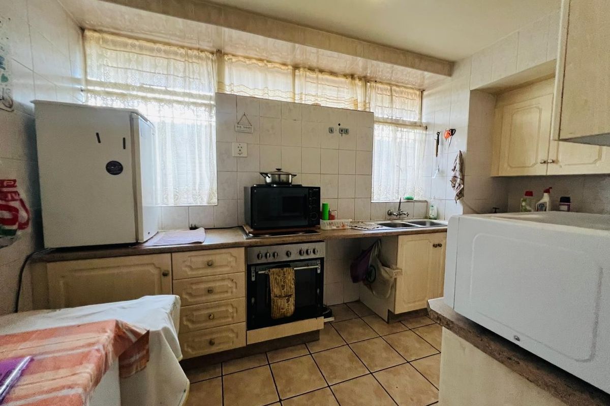 A functional kitchen featuring built-in cabinetry, tiled backsplash, and ceramic flooring, offering a dated aesthetic with potential for modern renovation.