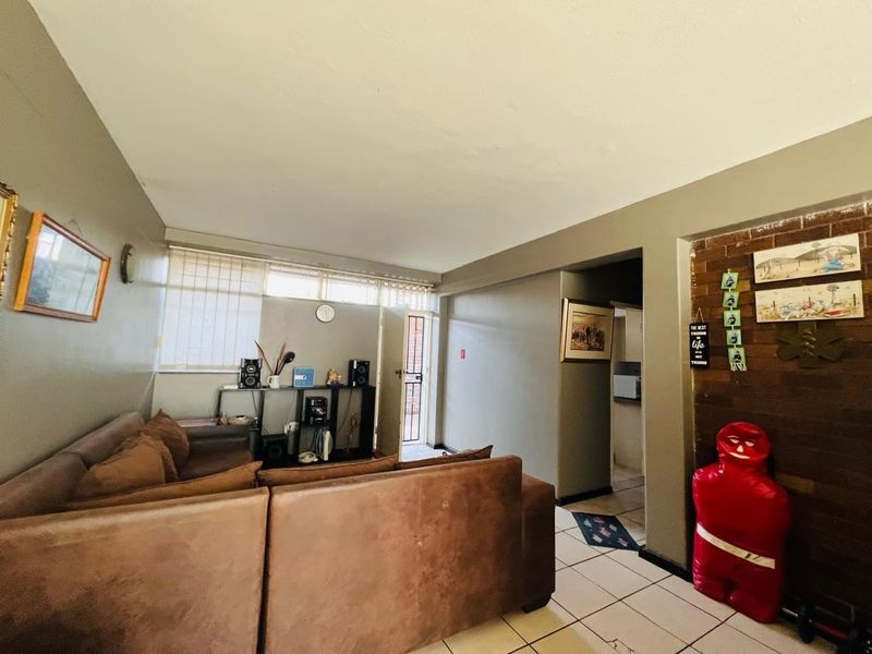 A living room featuring tiled flooring, an exposed brick accent wall, and access to an exterior entrance with a security gate.