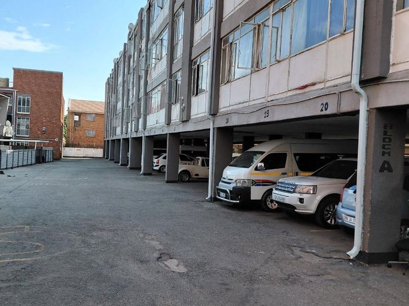 Exterior view of a multi-story apartment block featuring ground-level covered parking bays and a weathered concrete facade.