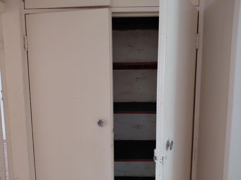 A built-in storage cupboard featuring multiple internal shelves, showing signs of wear and requiring cosmetic refurbishment.