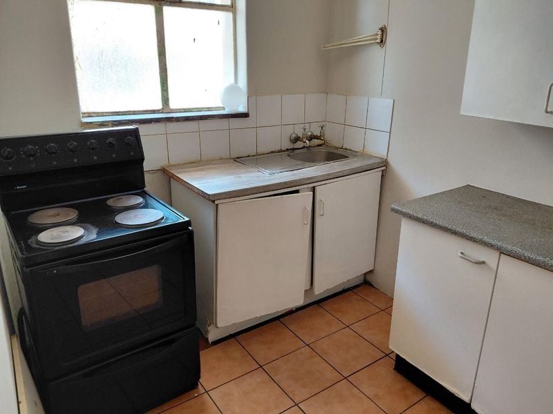 A compact kitchen featuring basic cabinetry, a stainless steel sink, tiled backsplash, and ceramic flooring, currently in need of renovation and modernization.