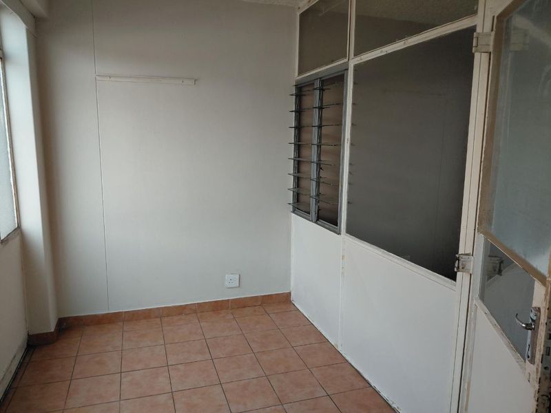 An empty, enclosed balcony or sunroom featuring tiled flooring, partitioned glass walls, and louvre windows, offering a blank canvas for renovation.